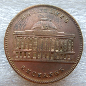 May include: A copper-colored coin with the words "MERCHANTS EXCHANGE" around the top and bottom. The coin features a detailed illustration of a building with a domed roof.