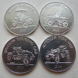 Puede incluir: Cuatro monedas conmemorativas plateadas con diseños de coches antiguos en relieve. Cada moneda muestra un modelo diferente: White Steamer 1901, Studebaker Electric 1902, Winton Touring Car 1903 y Autocar Type VIII 1904.