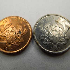 May include: Two Ghanaian coins, one copper and one silver, both featuring the national coat of arms with a star and two birds, and the year 2007.