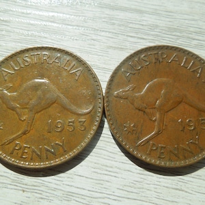 Puede incluir: Dos monedas de penique australianas de bronce de 1953. Cada moneda presenta un canguro y la palabra "AUSTRALIA" en la parte superior, con "PENNY" en la parte inferior. Las monedas muestran signos de desgaste, lo que indica que han estado en circulaci&oacute;n.