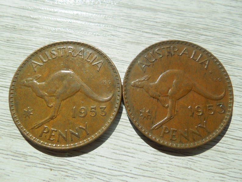 Puede incluir: Dos monedas de penique australianas de bronce de 1953. Cada moneda presenta un canguro y la palabra "AUSTRALIA" en la parte superior, con "PENNY" en la parte inferior. Las monedas muestran signos de desgaste, lo que indica que han estado en circulaci&oacute;n.