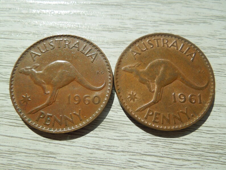 Puede incluir: Dos monedas de penique australianas de color cobre. Cada moneda presenta un canguro, la palabra "AUSTRALIA" en la parte superior y el a&ntilde;o de acu&ntilde;aci&oacute;n, 1960 o 1961, con la palabra "PENNY" en la parte inferior.