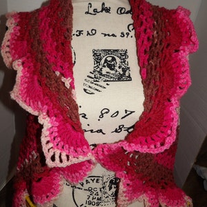 May include: A crocheted shawl in shades of pink, brown, and white. The shawl has a scalloped edge and is made with a delicate stitch.