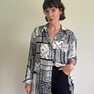 May include: A long-sleeved button-down shirt featuring a black and white patchwork pattern with various intricate geometric and floral designs. The shirt has a classic collar, a front button placket, and loose-fitting sleeves with cuffs.