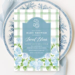 Op de afbeelding: Een rechthoekige uitnodigingskaart voor een babyshower met een groen-witte aquarel ruitjesachtergrond en blauwe hortensia-illustraties onderaan. Een centraal blauw ovaal kader bevat witte tekst, waaronder de naam Sarah Bloom.