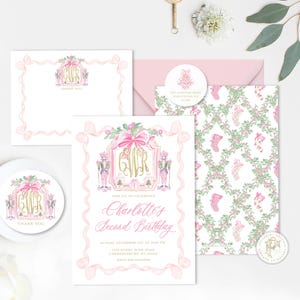 K&ouml;nnte beinhalten: Eine Sammlung von rosa und goldenen Schreibwaren, darunter eine Einladung, eine Dankeskarte, ein Umschlag und ein Aufkleber. Die Einladung tr&auml;gt den Text "Charlotte's Second Birthday" und zeigt Nussknacker, Schleifen und ein Monogramm.