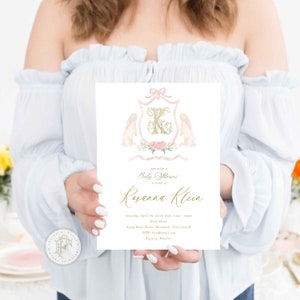 May include: A pink and gold baby shower invitation with a crest featuring a letter K, two bunnies, and floral accents. The text reads "Join us for a Baby Shower in honor of Rosanna Klein".