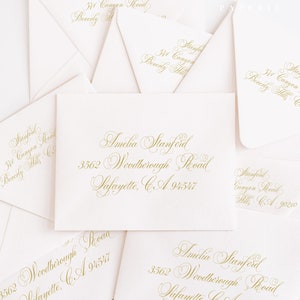 May include: A collection of ivory envelopes with gold calligraphy. The envelopes feature names, addresses, and the text "Freshmint Paperie." The calligraphy is in a flowing script, perfect for wedding invitations or announcements.