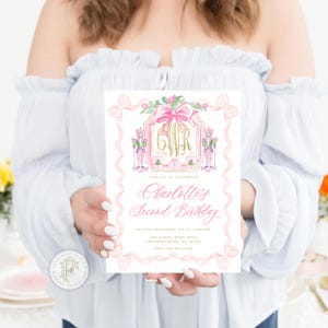 K&ouml;nnte beinhalten: Eine rosa-goldene Geburtstagseinladung mit Schleifen- und Nussknacker-Motiv. Auf der Einladung steht "Charlotte's Second Birthday" in eleganter Schrift. Das Design umfasst ein Monogramm und dekorative Elemente.