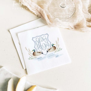 May include: White square paper napkins with a watercolor design featuring two ducks, a blue monogram, and the names "HUDSON ANDREW COLETTA." The napkins are part of a wedding stationery set.