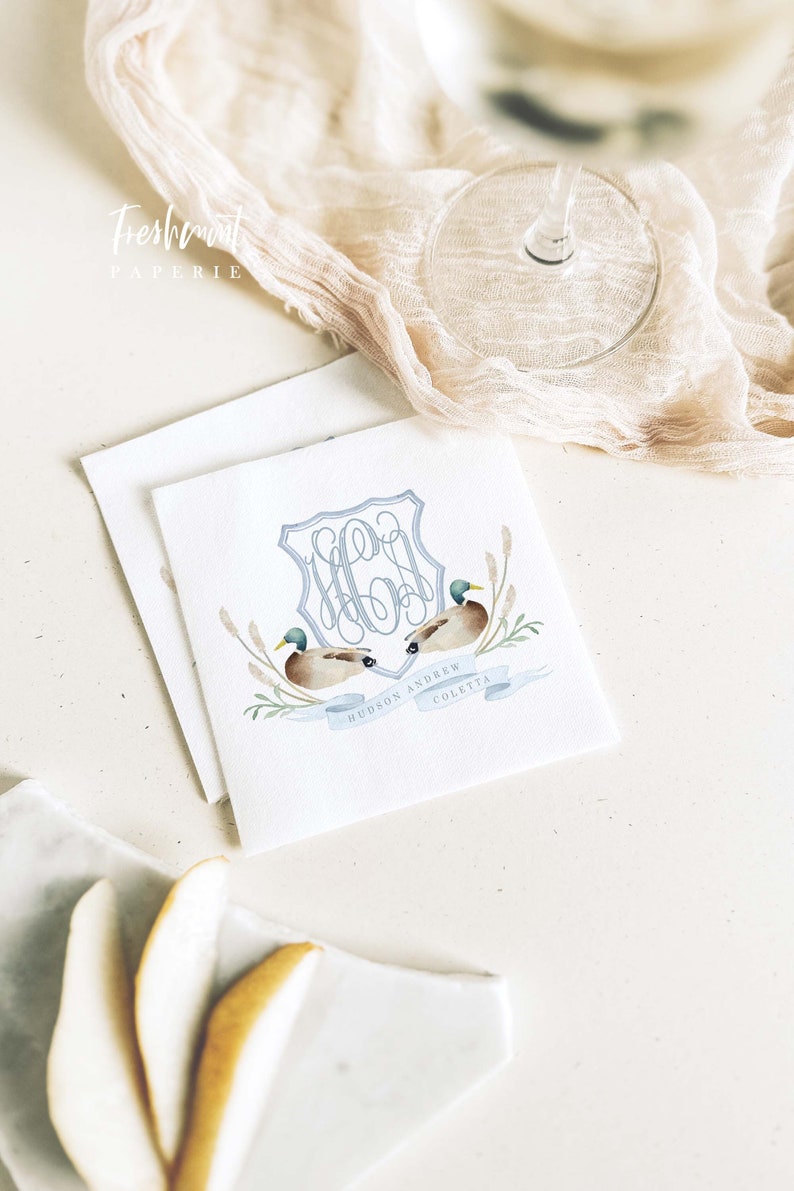 May include: White square paper napkins with a watercolor design featuring two ducks, a blue monogram, and the names "HUDSON ANDREW COLETTA." The napkins are part of a wedding stationery set.