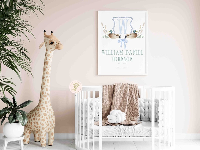 May include: A white crib with a brown blanket and white pillows. A stuffed giraffe stands next to the crib. A framed print with a blue and white monogram and the name "William Daniel Johnson" is on the wall.