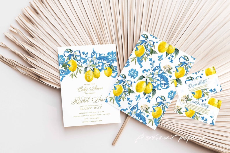 May include: A set of baby shower invitations with a lemon and floral design. The invitations are white with blue and gold accents. The text on the invitation reads "Join us for a Baby Shower in honor of Rachel Smith Celebrating the arrival of a Baby Boy".