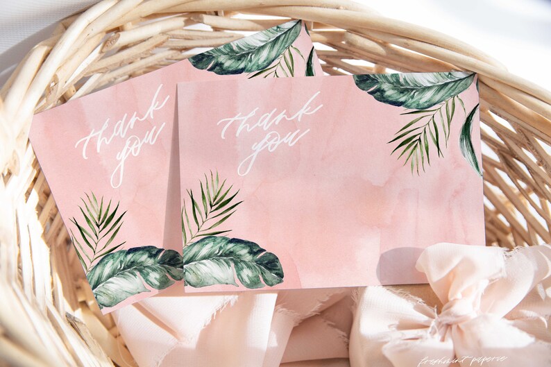 May include: Two pink thank you cards with green tropical leaf designs and white calligraphy. The cards are in a wicker basket with pink fabric.
