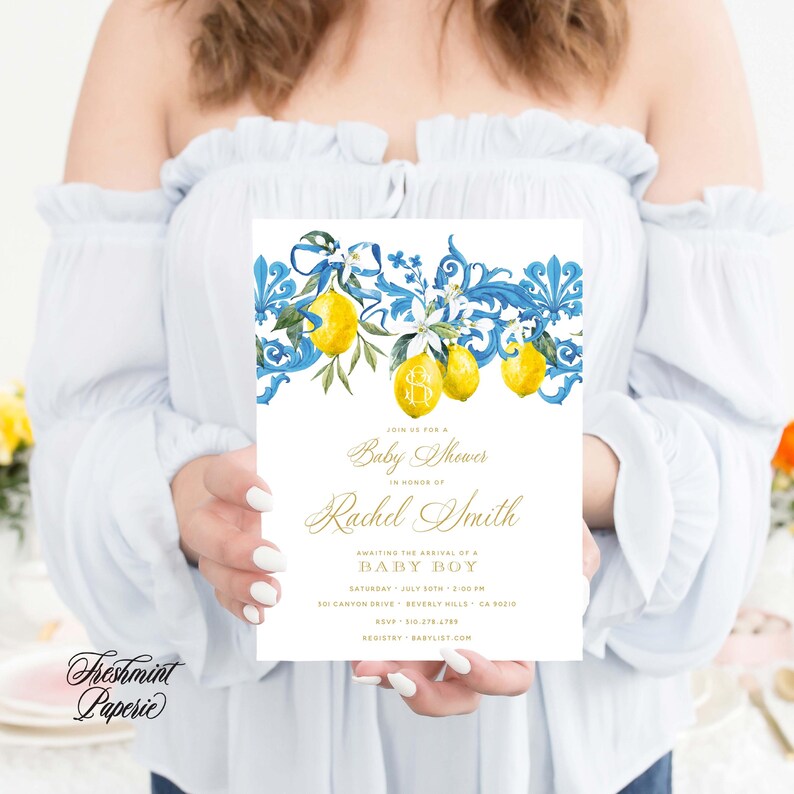 May include: A baby shower invitation with a blue and white floral design featuring lemons and a gold monogram. The invitation text reads "Join us for a Baby Shower in honor of Rachel Smith Awaiting the arrival of a Baby Boy Saturday, July 20th, 2:00 PM 301 Canyon Drive, Beverly Hills, CA 90210 RSVP: 555-555-5555 Registry: Babylist.com"