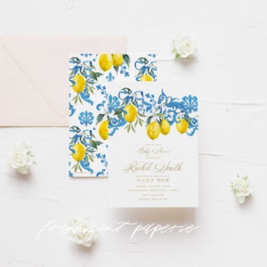 May include: A baby shower invitation with a blue and white tiled pattern featuring lemons and floral accents. The invitation text reads "You're Invited to a Baby Shower" and "Rachel Smith" in gold script. The text "Baby Boy" is in gold block letters.