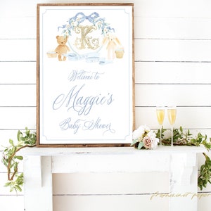 Op de afbeelding: Een houten bord met een blauw en gouden ontwerp met een teddybeer en een konijn. Het bord zegt "Welkom op Maggies Baby Shower".
