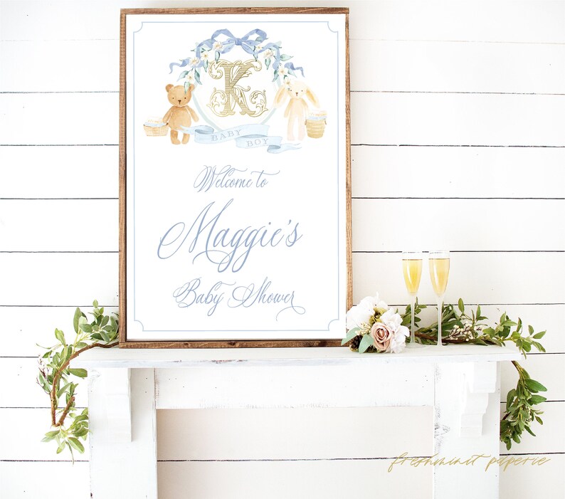Op de afbeelding: Een houten bord met een blauw en gouden ontwerp met een teddybeer en een konijn. Het bord zegt "Welkom op Maggies Baby Shower".