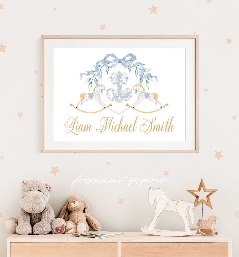 Peut inclure: Une affiche encadr&eacute;e avec un motif aquarelle. Elle pr&eacute;sente un n&oelig;ud bleu, des &eacute;l&eacute;ments floraux et deux chevaux &agrave; bascule. Le nom "Liam Michael Smith" est &eacute;crit en script dor&eacute;. Le fond est beige clair avec des &eacute;toiles.