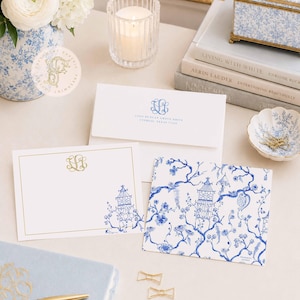 Peut inclure: Un ensemble de papeterie comprenant des cartes et enveloppes blanches avec des motifs à l'encre bleue et dorée. Une carte présente un monogramme doré et une pagode bleue. Une enveloppe porte un monogramme bleu. Une carte à motif floral bleu est incluse.