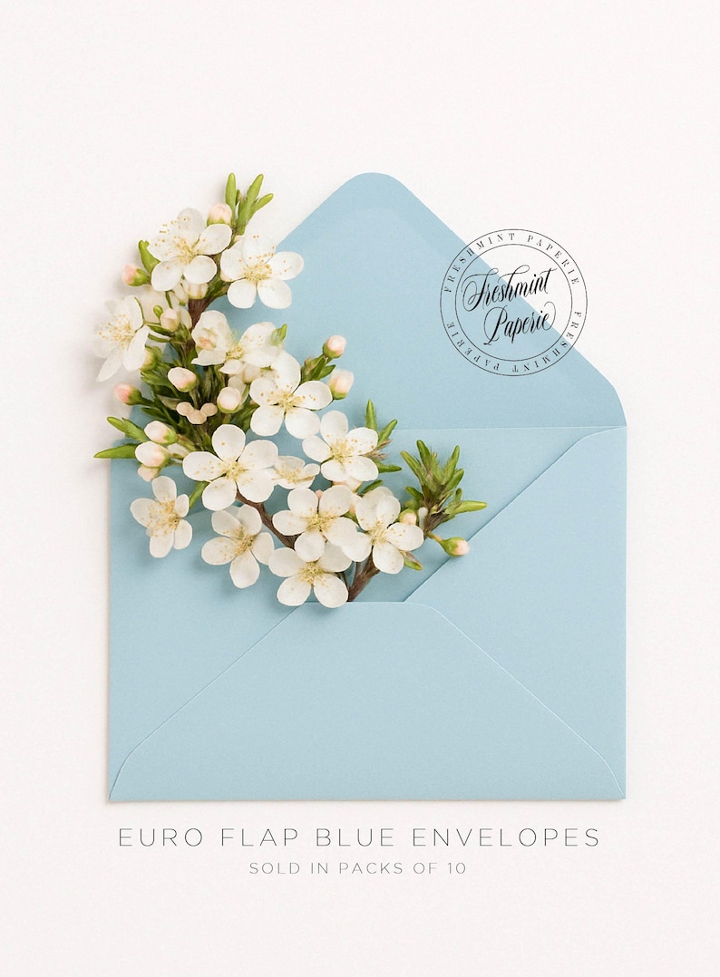 May include: A light blue envelope with a white flower tucked inside. The envelope has a round sticker with the text "Freshmint Paperie" in a cursive font. The text below the envelope reads "EURO FLAP BLUE ENVELOPES SOLD IN PACKS OF 10".