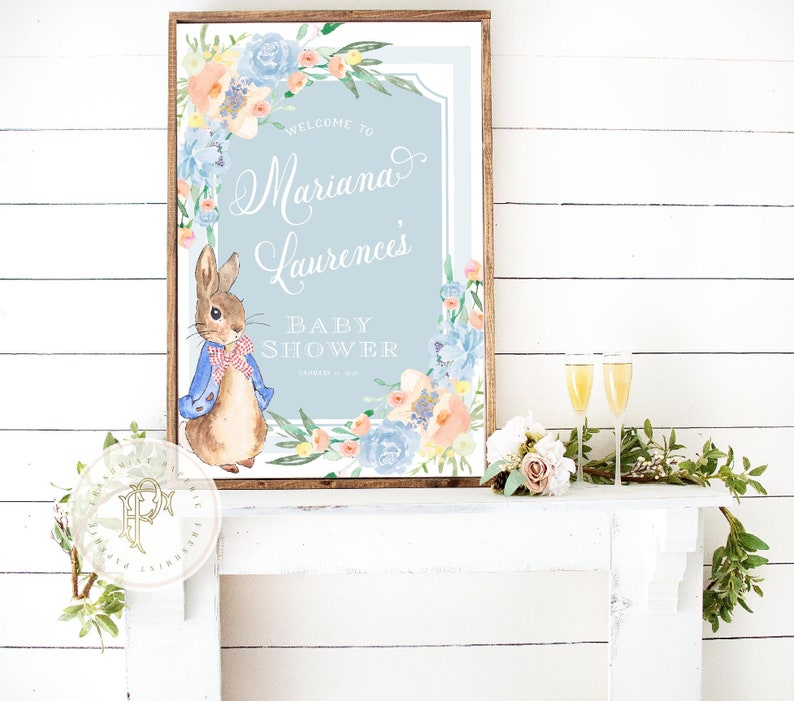 May include: A blue and white baby shower sign with a watercolour floral border and a cartoon rabbit. The sign says "Welcome to Mariana Laurence's Baby Shower".