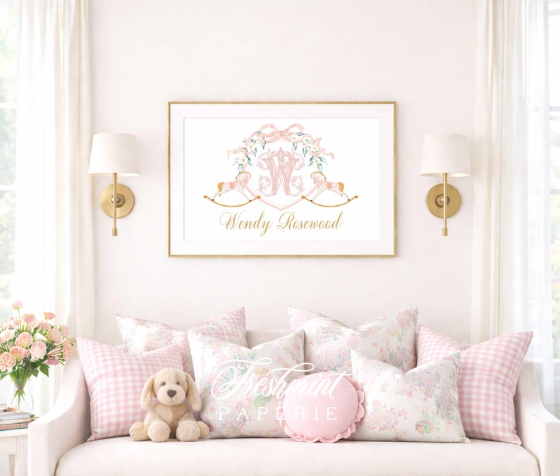 May include: A framed print with a gold border featuring a pink and gold design with the name "Wendy Rosewood". The print is above a white couch with pink pillows and a stuffed dog. The room has white curtains and gold sconces.