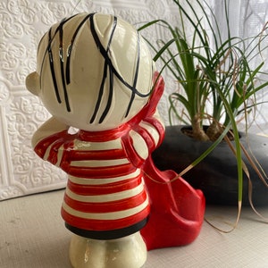 May include: A ceramic figurine of a child holding a red guitar. The child is wearing a red and white striped shirt and black trousers. The figurine is painted in a whimsical style.