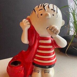May include: A ceramic figurine of a boy wearing a red scarf and a striped shirt. The figurine is holding a red candle holder.