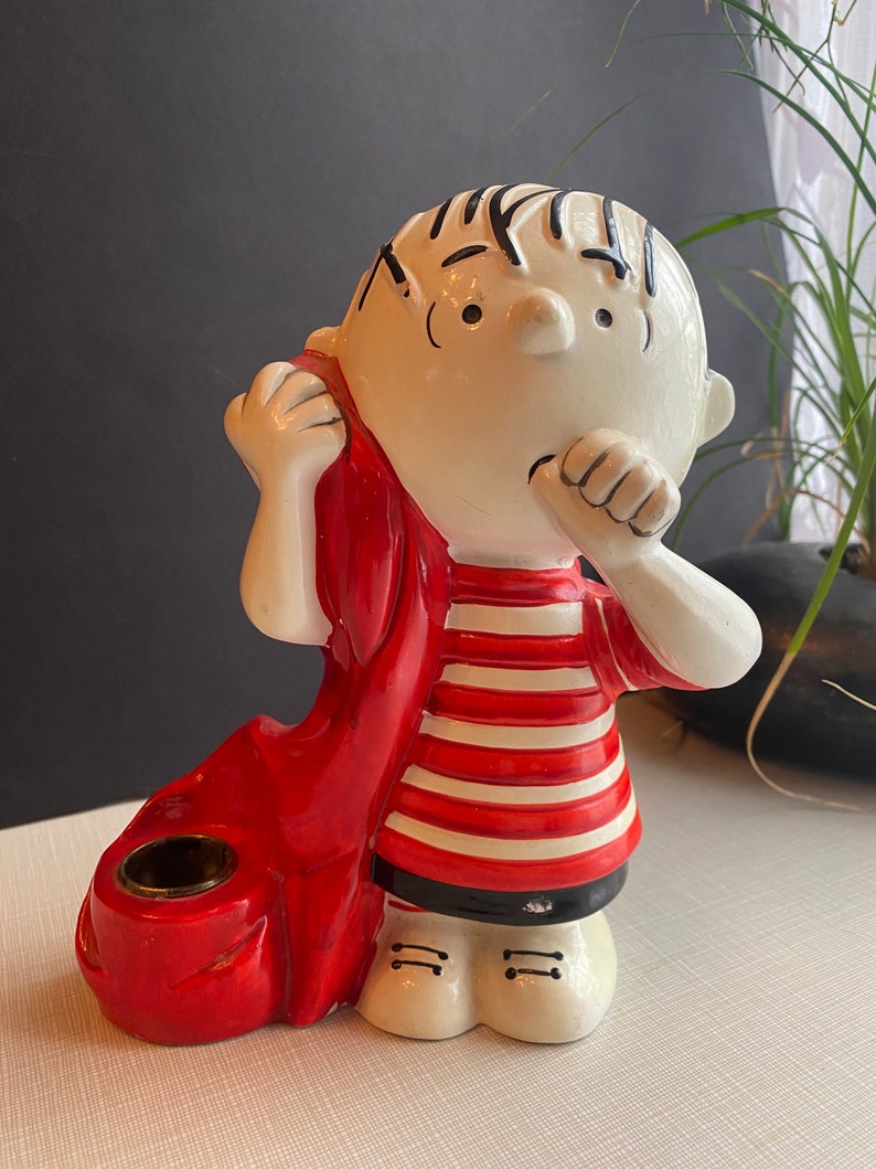 May include: A ceramic figurine of a boy wearing a red scarf and a striped shirt. The figurine is holding a red candle holder.