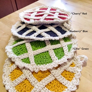 Pode incluir: Quatro panos de cozinha de crochê em forma de crosta de torta. Os panos de cozinha são sobrepostos, com a camada superior vermelha, a segunda camada azul, a terceira camada verde e a camada inferior amarela. Os panos de cozinha são etiquetados com as cores "Cereja" Vermelho, "Mirtilo" Azul, "Lima" Verde e "Limão" Amarelo.