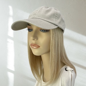 May include: A light beige baseball cap with a curved brim. The cap is made of a soft, textured fabric and has a classic six-panel design. The cap is displayed on a mannequin with blonde hair and a white shirt.
