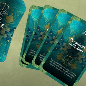 Może przedstawiać: Zestaw kart orakulum z turkusowym i złotym wzorem. Karty przedstawiają astrologiczny symbol Wagi i tekst "The Oracle of Libra" oraz "Creativity in Action".