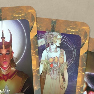 May include: Three illustrated cards with gold frames and ornate designs. The first card features a person with a crown and the word "Balder" at the bottom. The second card features a woman with a headdress and a long, flowing gown. The third card features a man with a beard and a fur-lined garment.