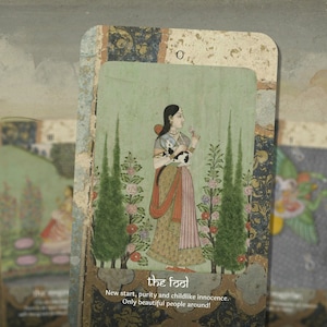 May include: A vintage tarot card depicting The Fool, a woman holding a white cat in a garden setting. The card has a green background with pink flowers and two green trees. The text on the card reads "The Fool" and "New start, purity and childlike innocence. Only beautiful people around!"