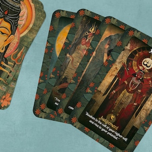 May include: A tarot deck with a green and gold background featuring a colorful illustration of a deity with multiple arms. The card is labeled "Judgement" and has the number "XX" in the top right corner. The text below the illustration reads "Awaken to the call of your higher self and rise to your potential."