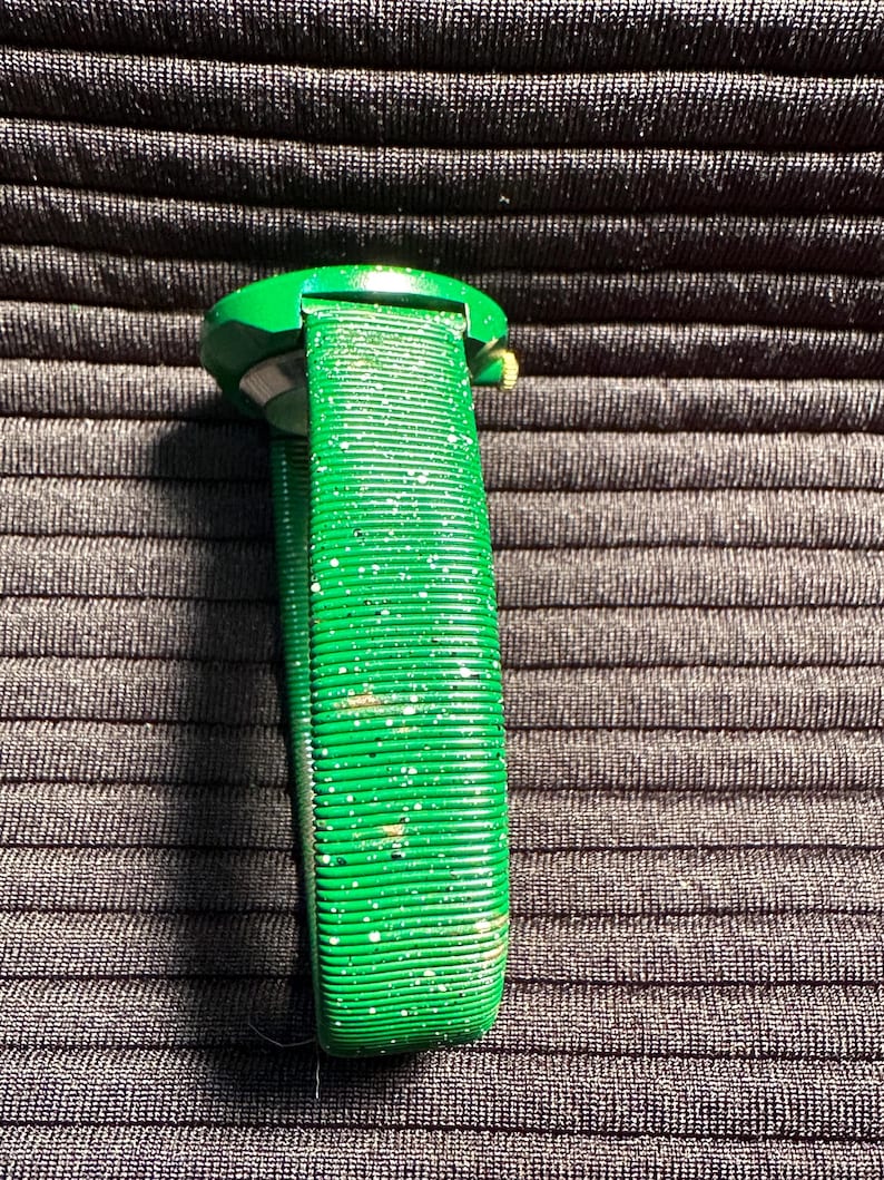 May include: A green watch with a sparkly green band. The watch face is round and has a gold rim.
