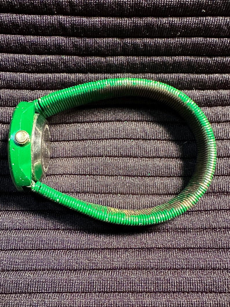 May include: A green watch with a green metal band. The watch face is round and has a gold-colored bezel.