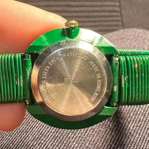 May include: A green wristwatch with a stainless steel back. The watch face is silver and has the text "Marlboro Made in Hong Kong" and "Stainless Steel Back".