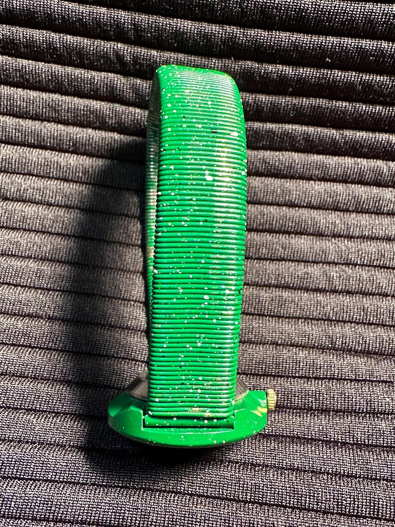 May include: A green watch with a sparkly green band. The watch face is round and has a gold accent.