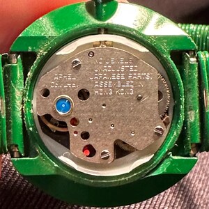 May include: A green round watch with a silver face and a gold crown. The watch face has the text "17 Jewels Stainless Steel Japanese Parts Assembled in Hong Kong".
