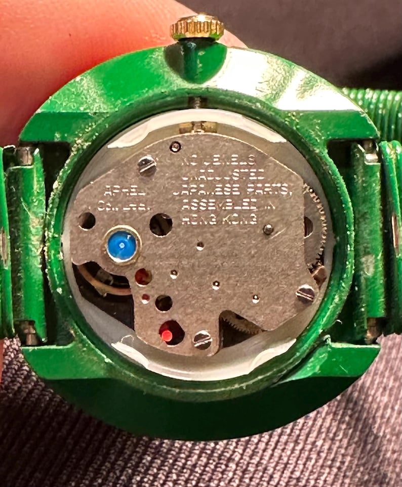 May include: A green round watch with a silver face and a gold crown. The watch face has the text "17 Jewels Stainless Steel Japanese Parts Assembled in Hong Kong".