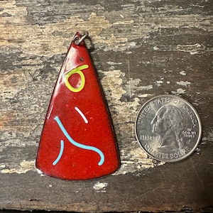 May include: Red enamel pendant with a yellow and blue design. The pendant is shaped like a triangle and has a silver loop at the top.