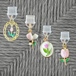 May include: Four clip-on earrings with floral designs. One earring features a gold oval frame with a pink tulip. Other earrings have pink and white flowers, and a pink tulip with green leaves. The clips are clear plastic.