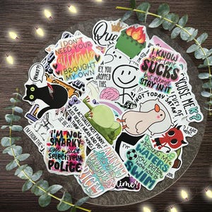 May include: A collection of colorful stickers with various designs and text. The stickers feature phrases like "I don't need your attitude," "Excuse me?" and "Testing my waters." Other designs include a black cat, a frog, and a hamster.