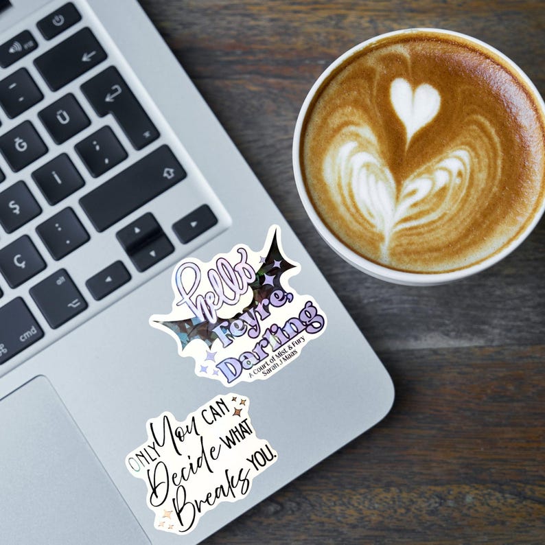 K&ouml;nnte beinhalten: Zwei Vinyl-Aufkleber auf einem Laptop. Der obere Aufkleber hat die Form eines Fledermausfl&uuml;gels mit violettem und wei&szlig;em Text "Hello Feyre, Darling" und "A Court of Mist & Fury Sarah J. Maas". Der untere Aufkleber zeigt den schwarzen Text "Only You Can Decide What Breaks You".
