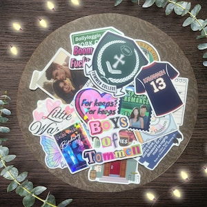 May include: A collection of stickers with various designs, including a football emblem, a jersey with "Kavanagh 13", and the text "Boys of Tommen". Other stickers feature book covers and romantic imagery. The stickers are arranged on a clear, round surface.