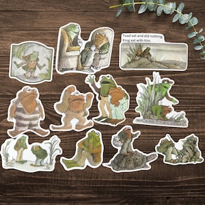 Puede incluir: Una colecci&oacute;n de pegatinas ilustradas con ranas antropom&oacute;rficas en varias escenas. Las pegatinas representan ranas en diferentes poses y entornos, algunas con texto. La paleta de colores incluye tonos de verde, marr&oacute;n y beige.