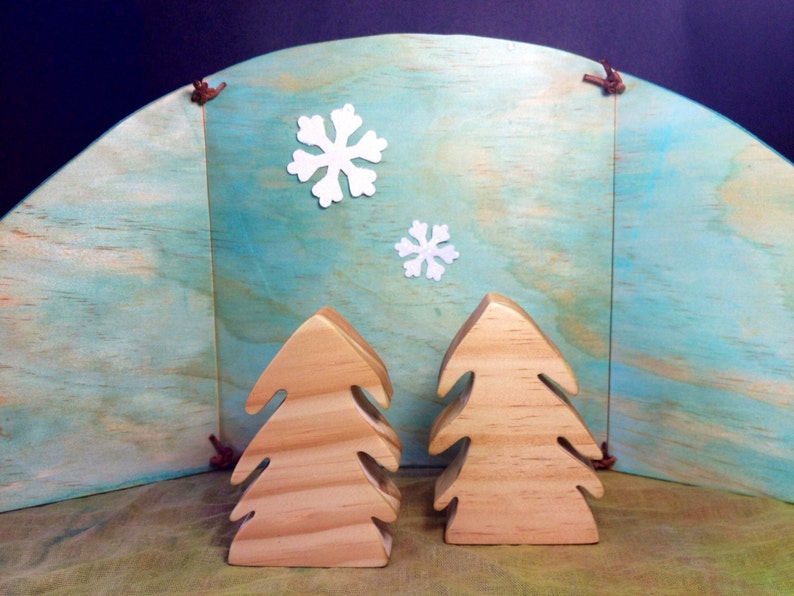 以下が含まれることがあります： 青と白の背景に、木製のクリスマスツリーが2本あります。背景は木目調で、白い紙の雪片が飾られています。
