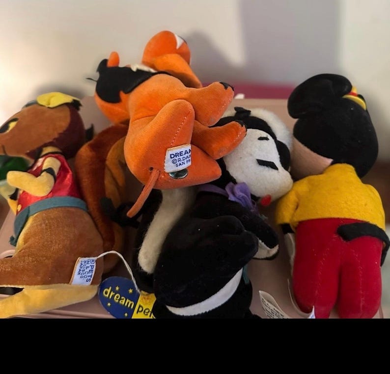 Pu&ograve; includere: Una collezione di peluche in vari colori. I giocattoli includono un personaggio marrone e giallo, un personaggio arancione e nero, un personaggio bianco e nero e un personaggio con una camicia gialla e pantaloni rossi. Alcuni giocattoli hanno etichette con la scritta "dream pets".